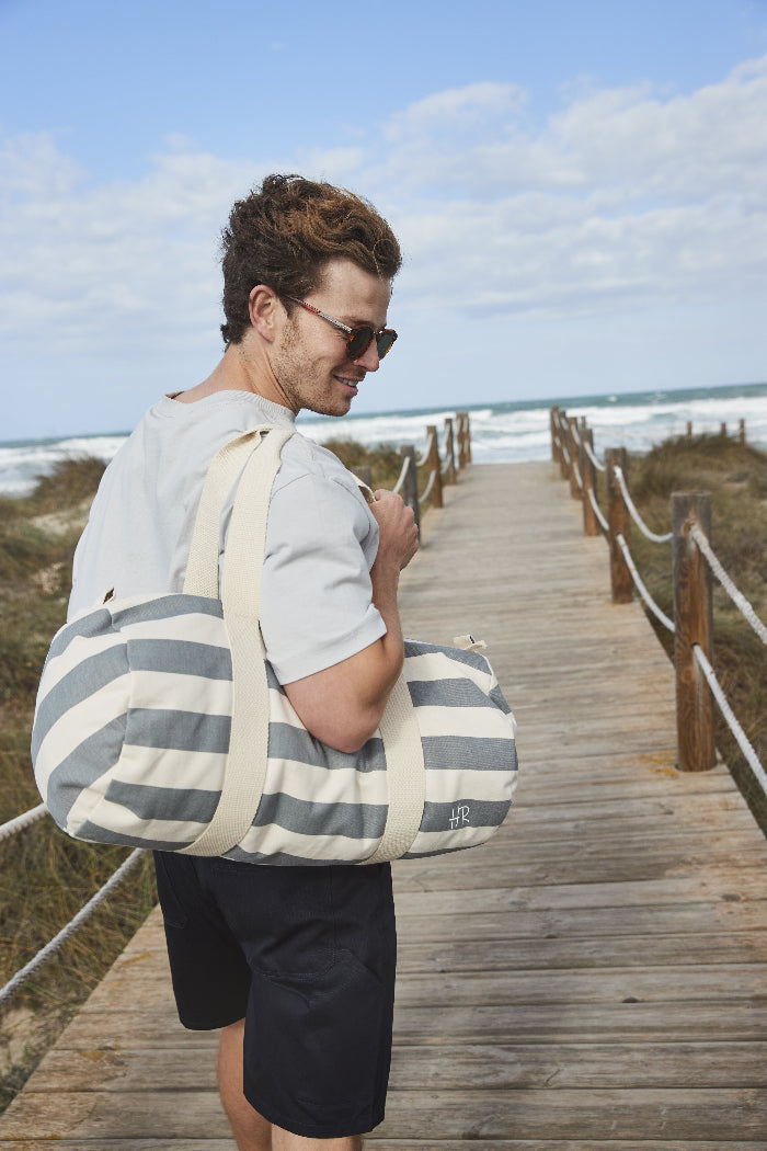 Knappe man op het strand met een hippe gepersonaliseerde barrel bag de uniekste strandtas als geschenk voor mannen of vrouwen van het merk kletskop