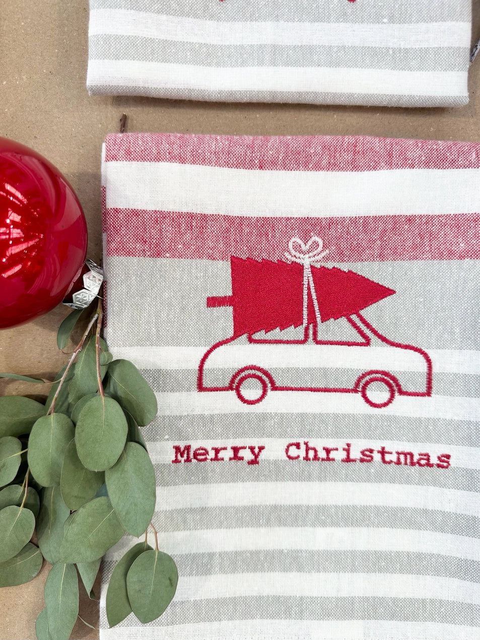 Geborduurde keukenhanddoek in kerstthema met een auto en kerstboom op het dak, origineel kerstgeschenk.