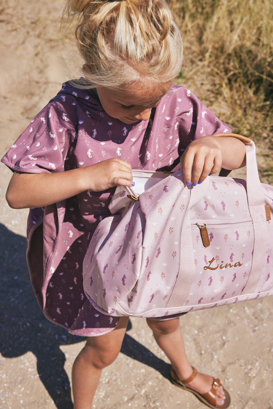 Meisje op het strand met gepersonaliseerde weekendtas van het Design merk Fresk. Stijlvol op naam geborduurd door Kletskop met een vrolijke zeepaardjes print